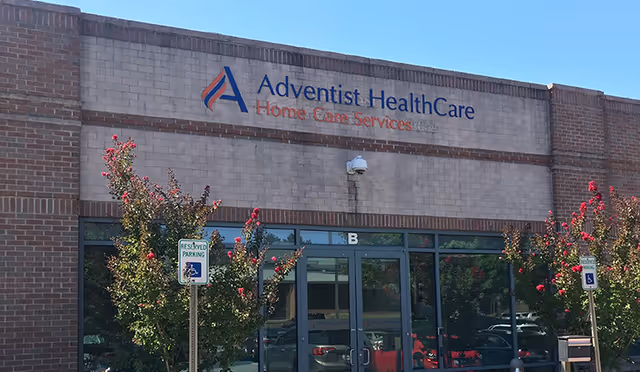 Facade of Adventist HealthCare Home Care Services building with glass doors and flowering trees.
