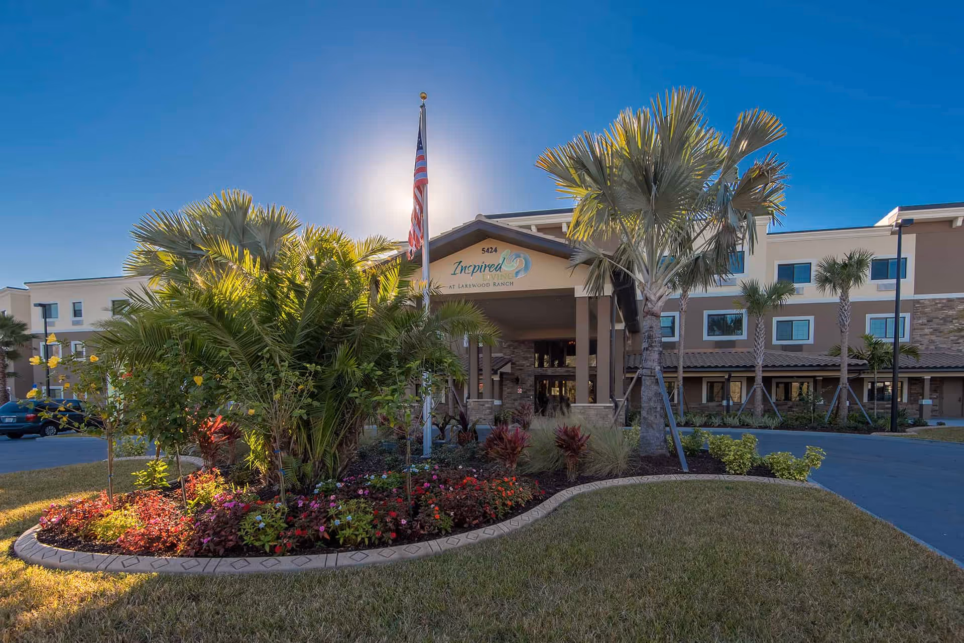 Exterior view of Inspired Living Lakewood Ranch entrance with tropical landscaping and flag.