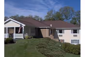 Exterior of a single-story beige nursing home with a brown roof, porch, and flag.