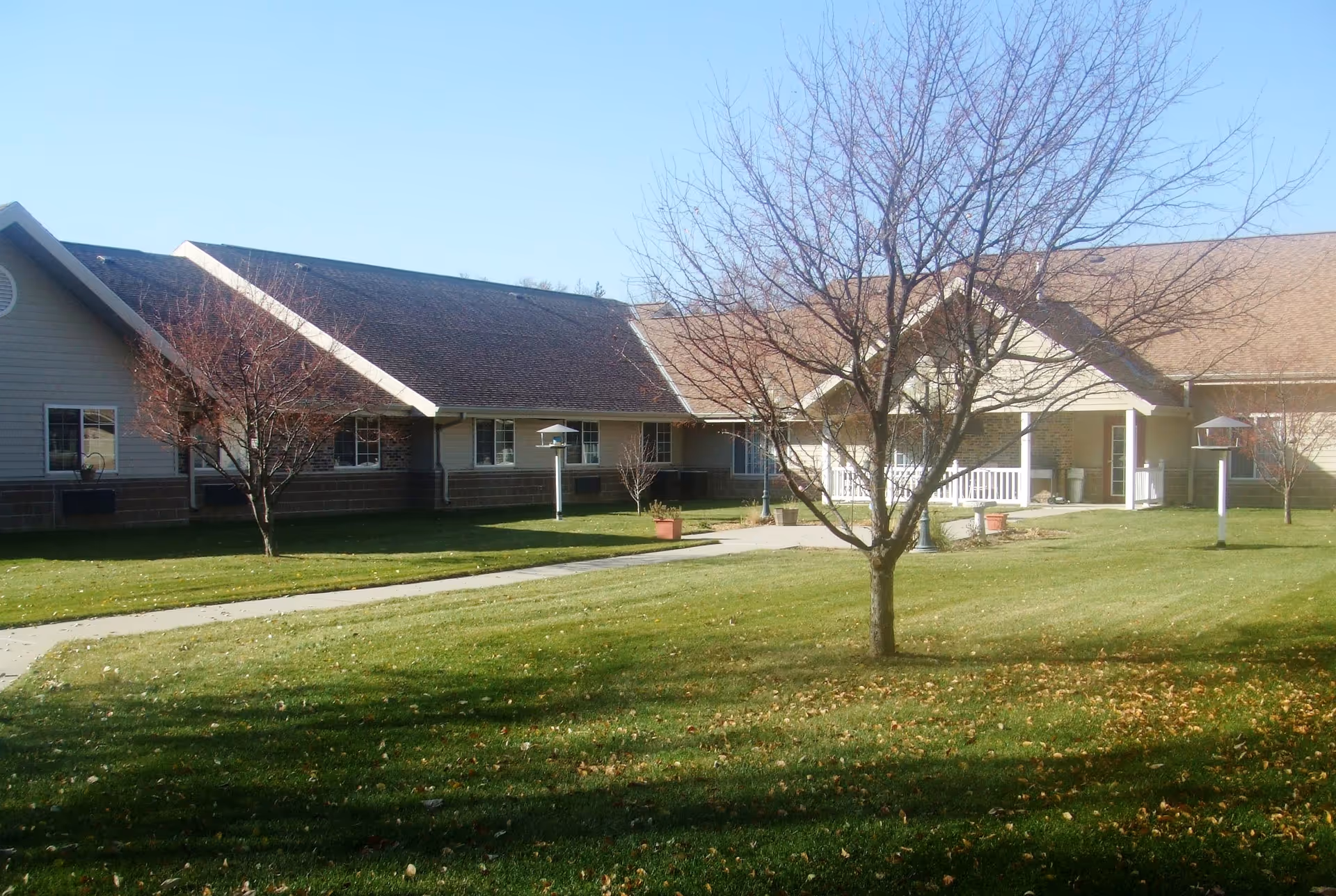 Single-story assisted living facility with a manicured lawn, leafless trees, and a welcoming front entrance.