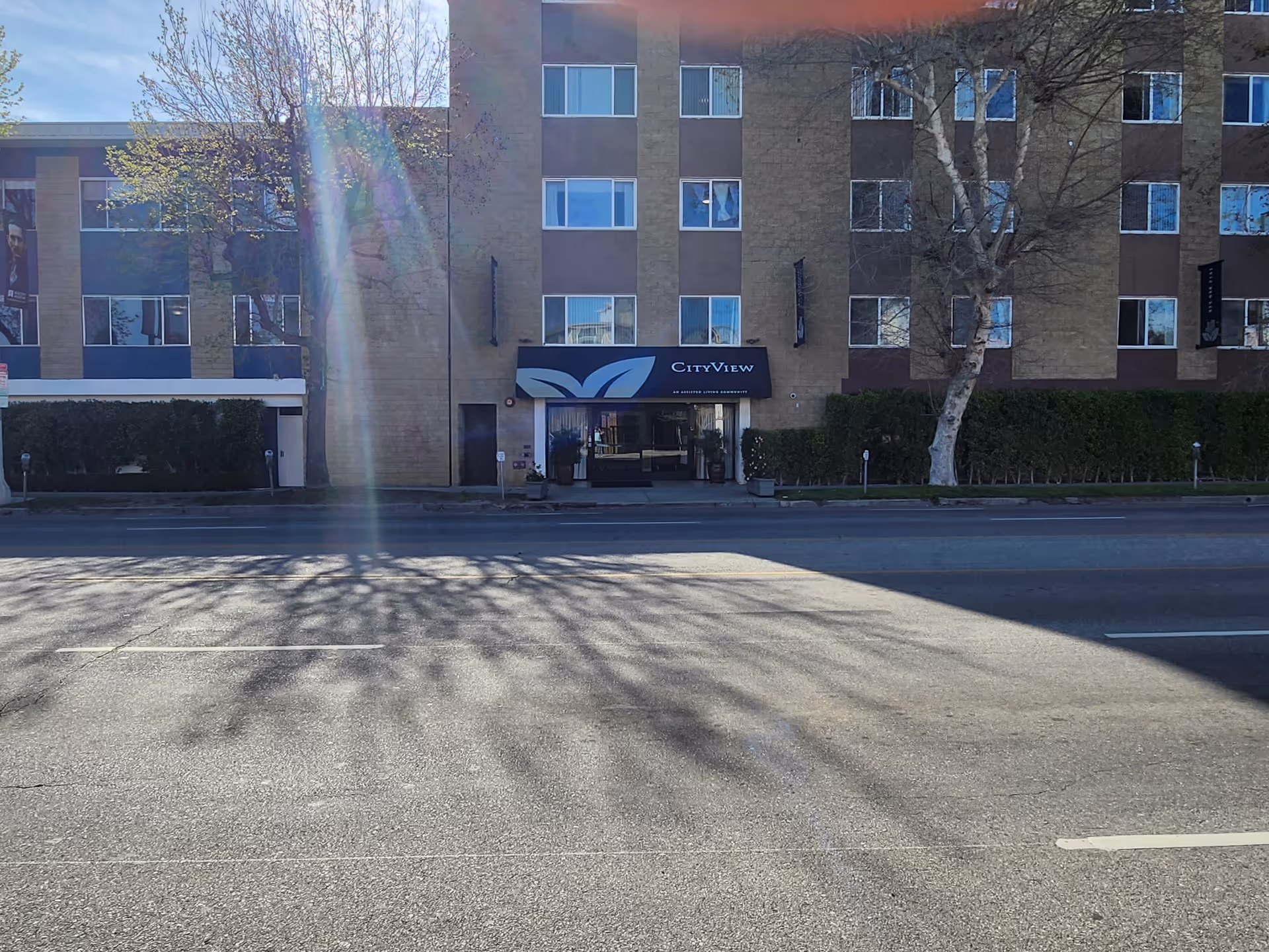 CityView senior living building entrance with a blue sign along a tree-lined street