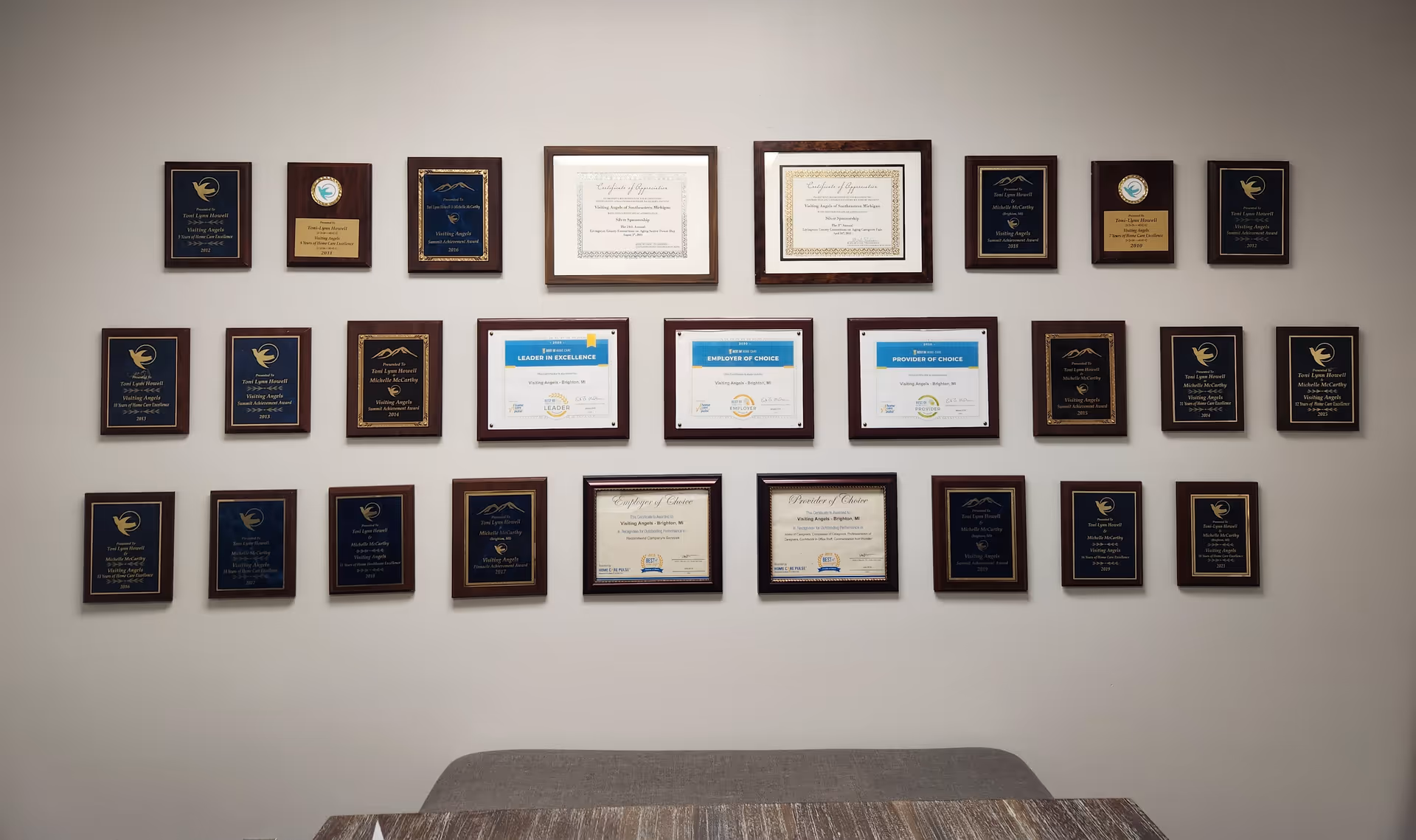 Wall filled with framed awards and certificates above a wooden table.