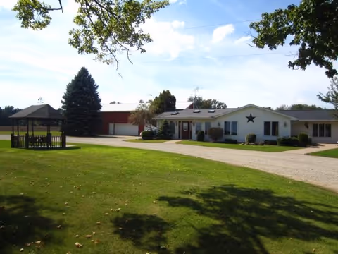 Country Meadows Care Home exterior with a gravel driveway, green lawn, and a gazebo.