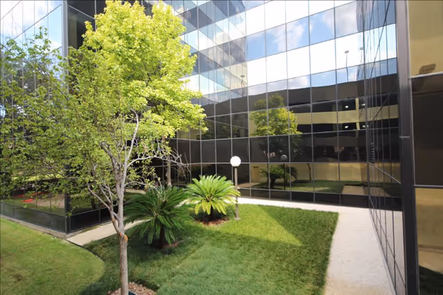 Exterior of a modern glass building with a small green courtyard.