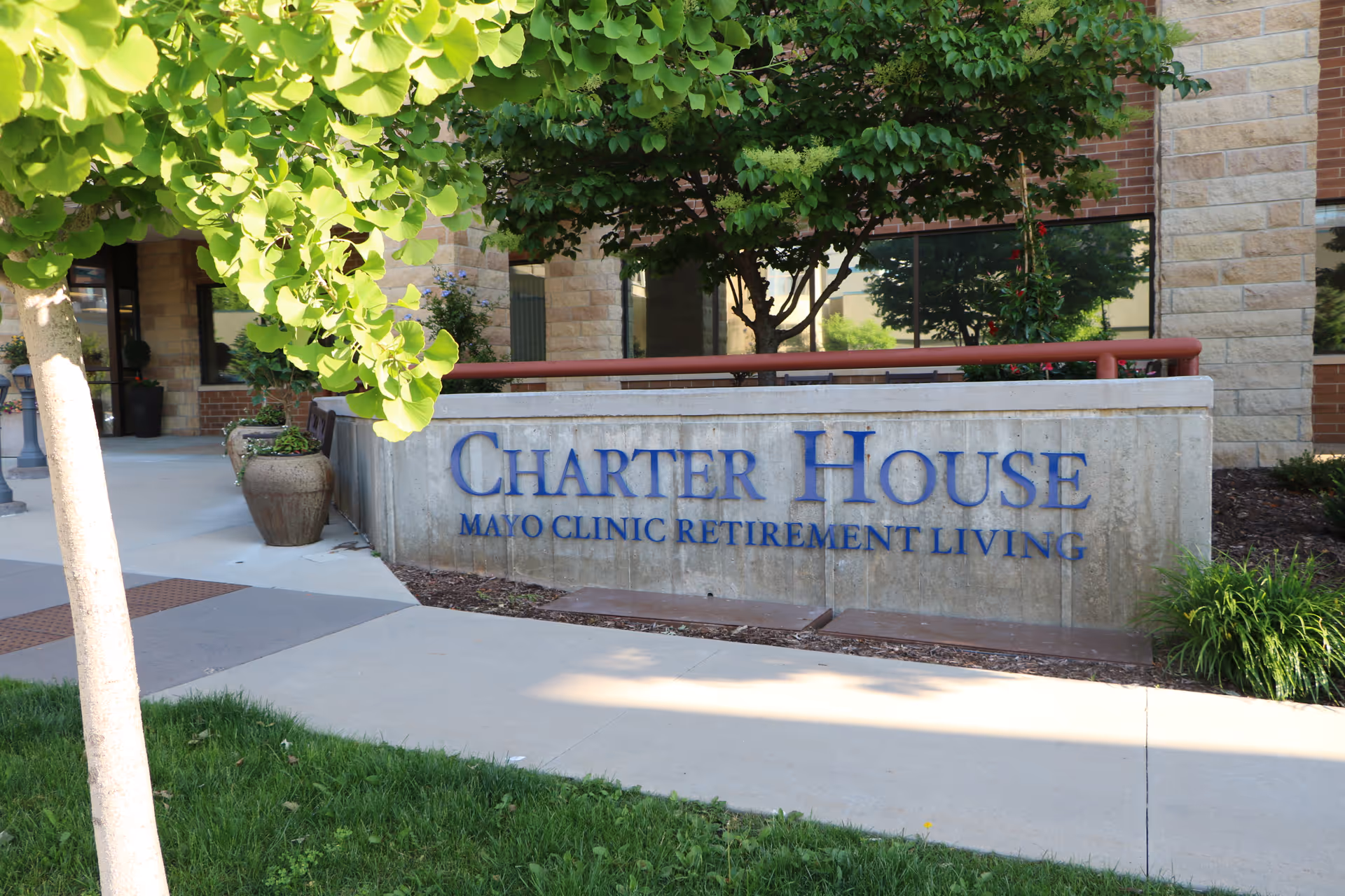 Exterior view of Charter House sign reading Mayo Clinic Retirement Living beside greenery.
