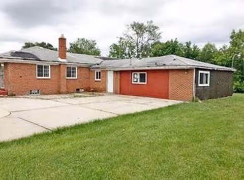 Single-story brick senior living facility exterior with driveway and grassy lawn.