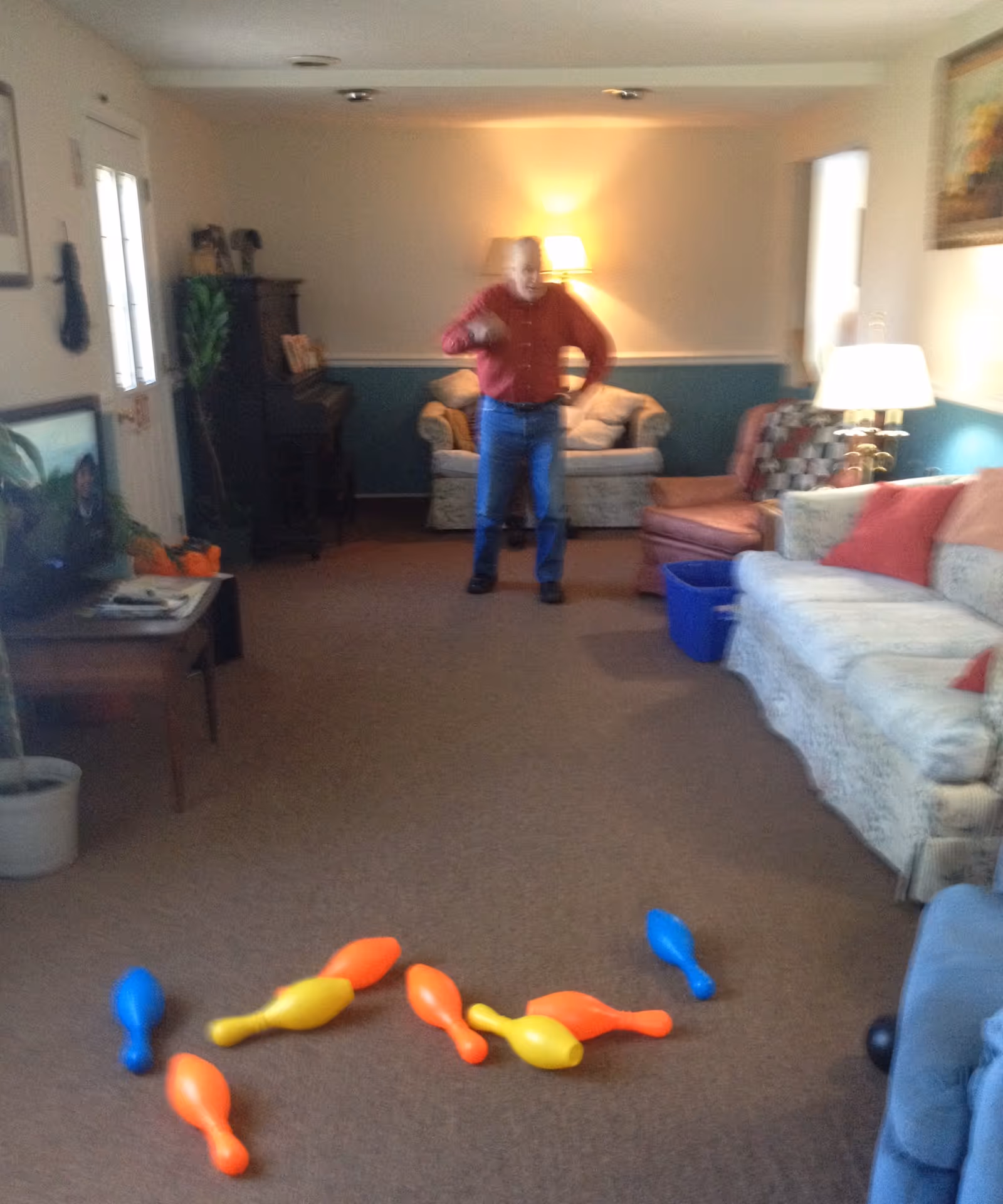 Senior man stands in a cozy living room with colorful bowling pins on the floor