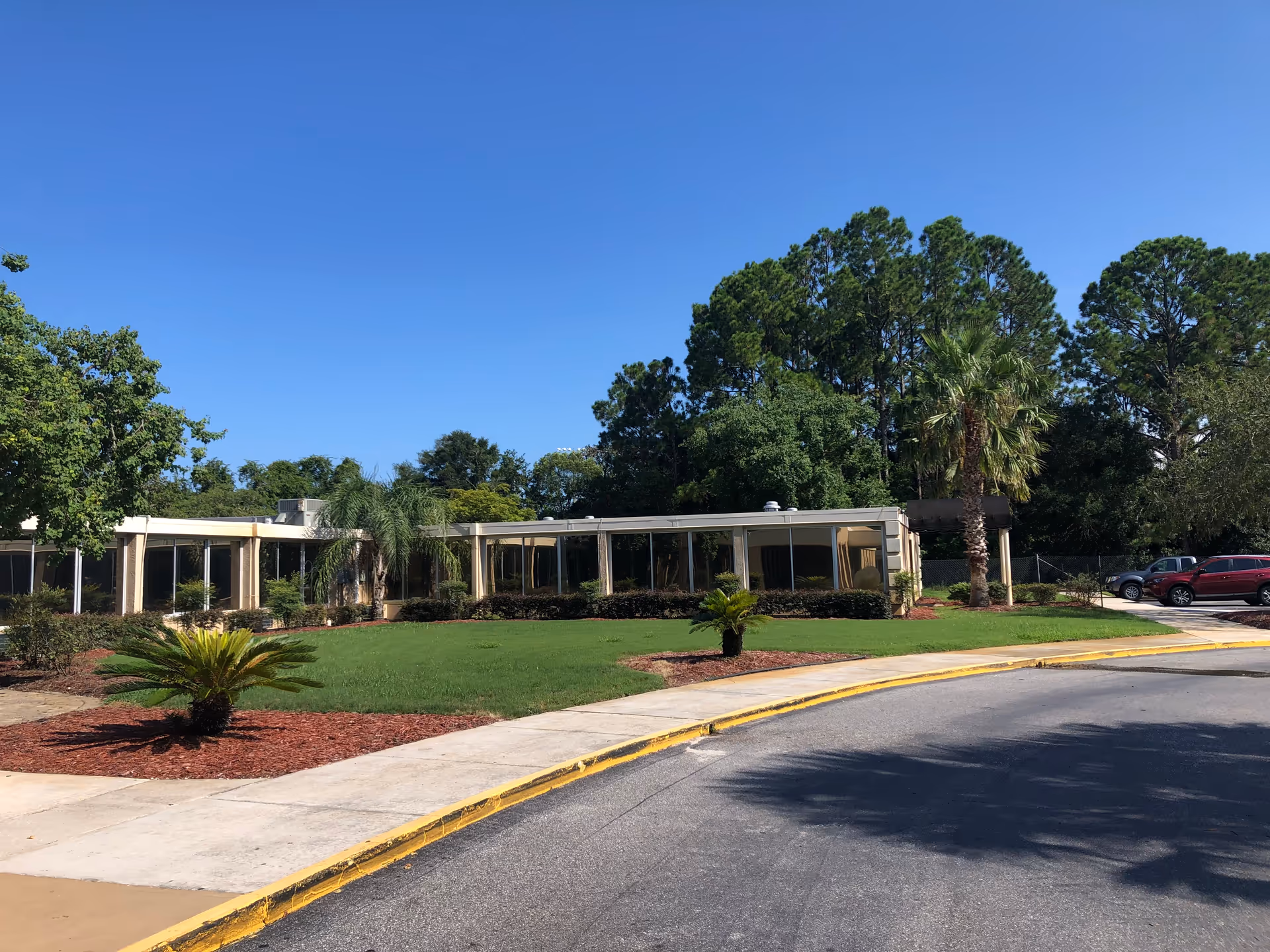 Exterior view of a single-story senior living center with glass walls and manicured landscaping.