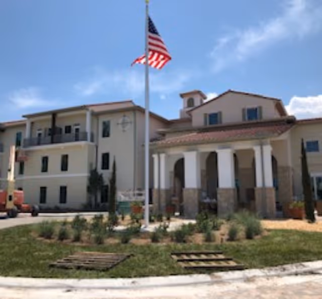 Facade of a Tuscan Gardens senior living building with flagpole and landscaped front yard.