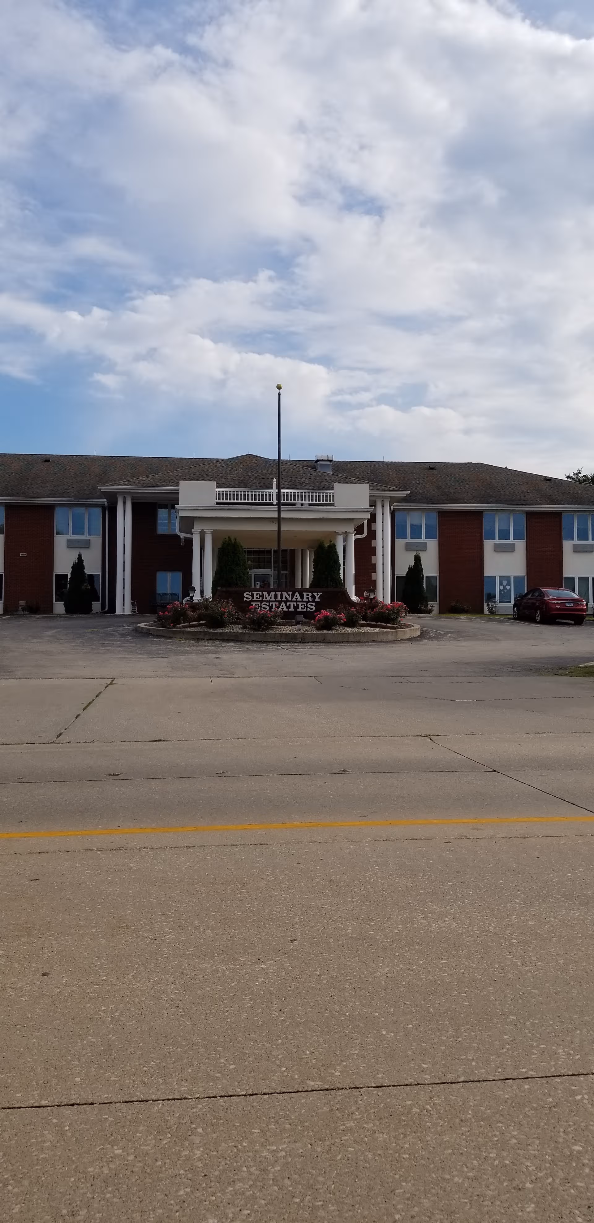 Front view of Seminary Estates senior living facility with landscaped entrance and parked car.
