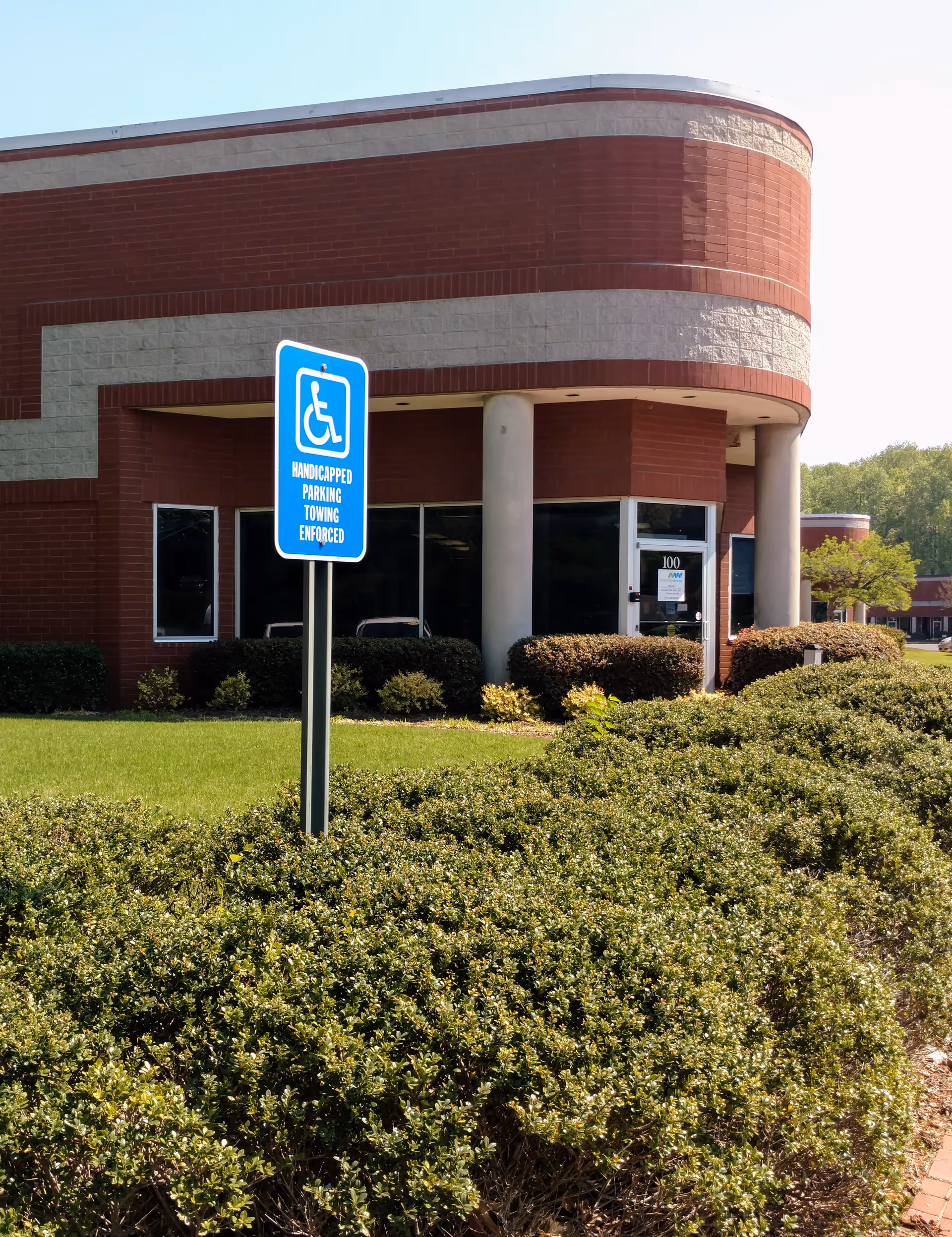 Red brick senior living facility entrance with blue handicap parking sign and landscaping.