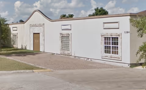 White single-story building with decorative curved roofline and multiple windows, no people present.