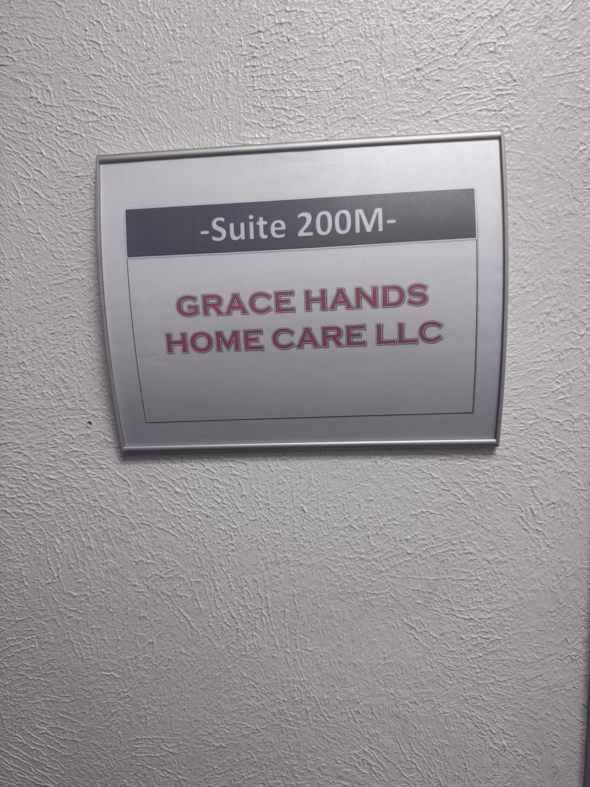 Metal plaque on a textured exterior wall reads 'Grace Hands Home Care LLC'.