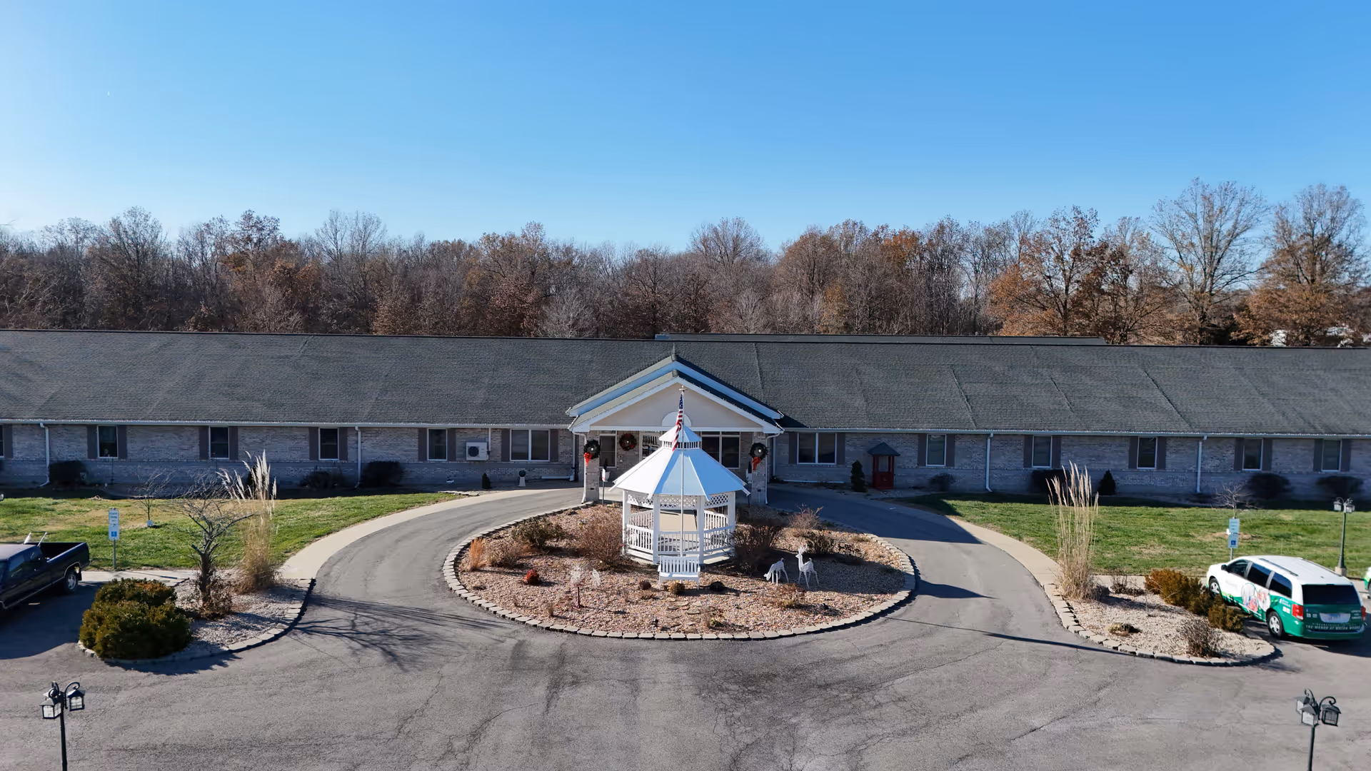 Front exterior of a single-story senior living facility with circular driveway and central gazebo.