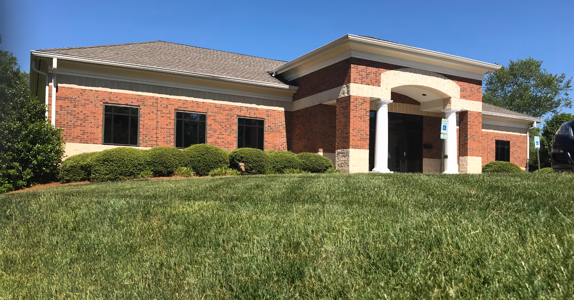 Brick senior living facility exterior with entrance columns and well-kept green lawn