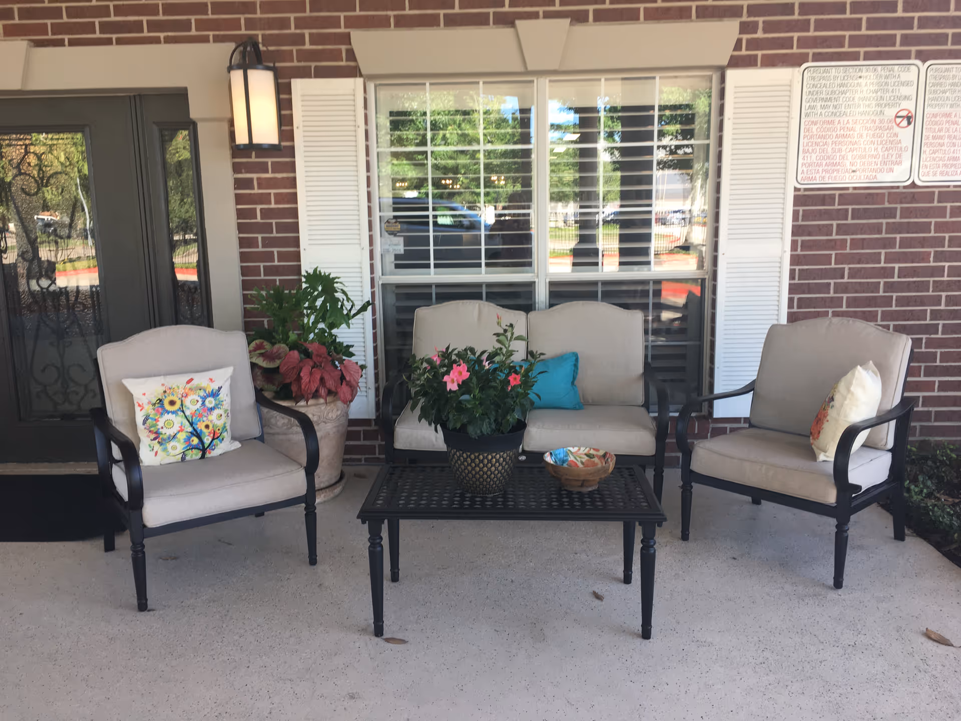 Patio seating area with beige cushioned chairs, a black table, and potted plants.