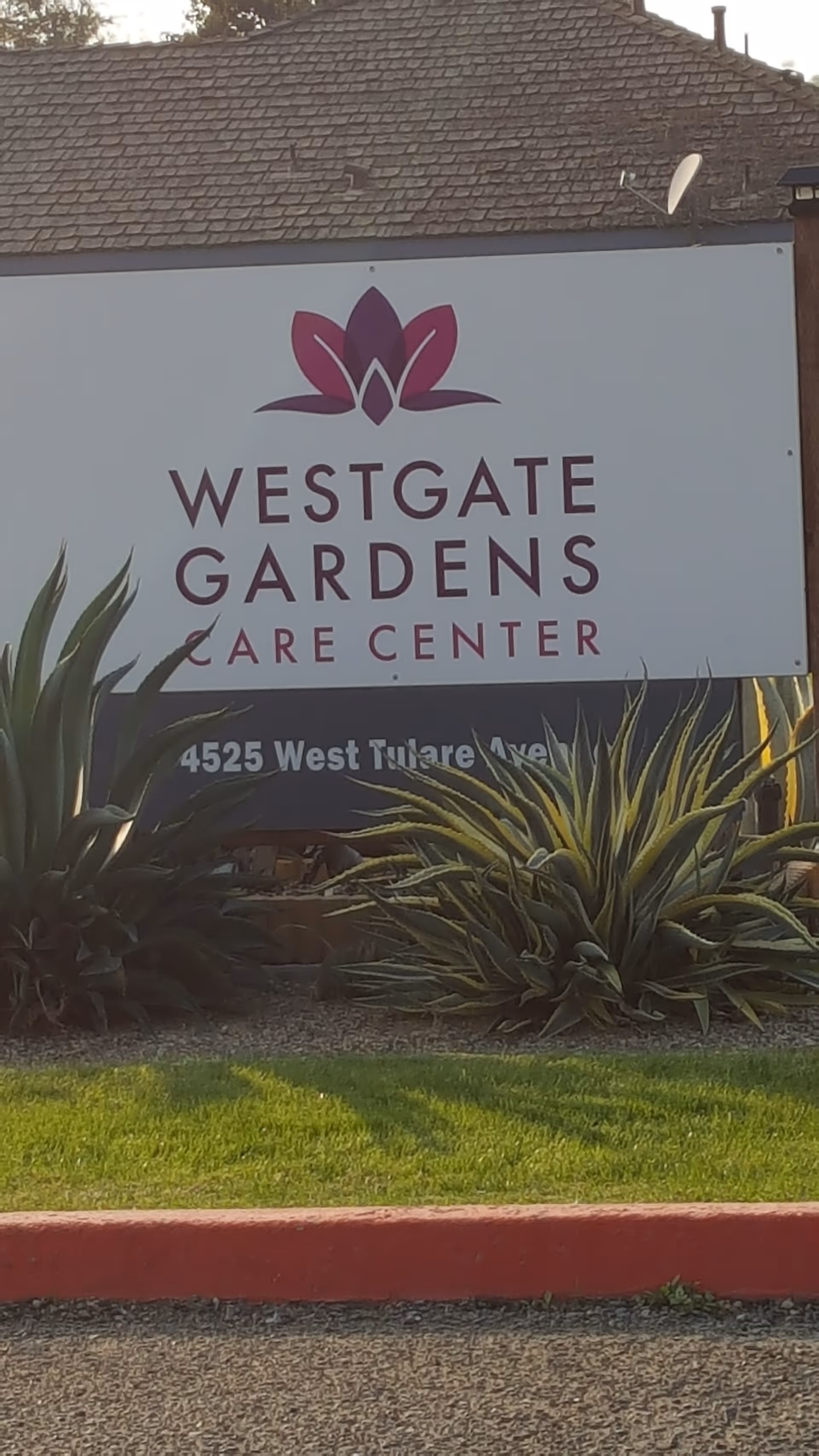 An outdoor sign for Westgate Gardens Care Center with spiky plants nearby.