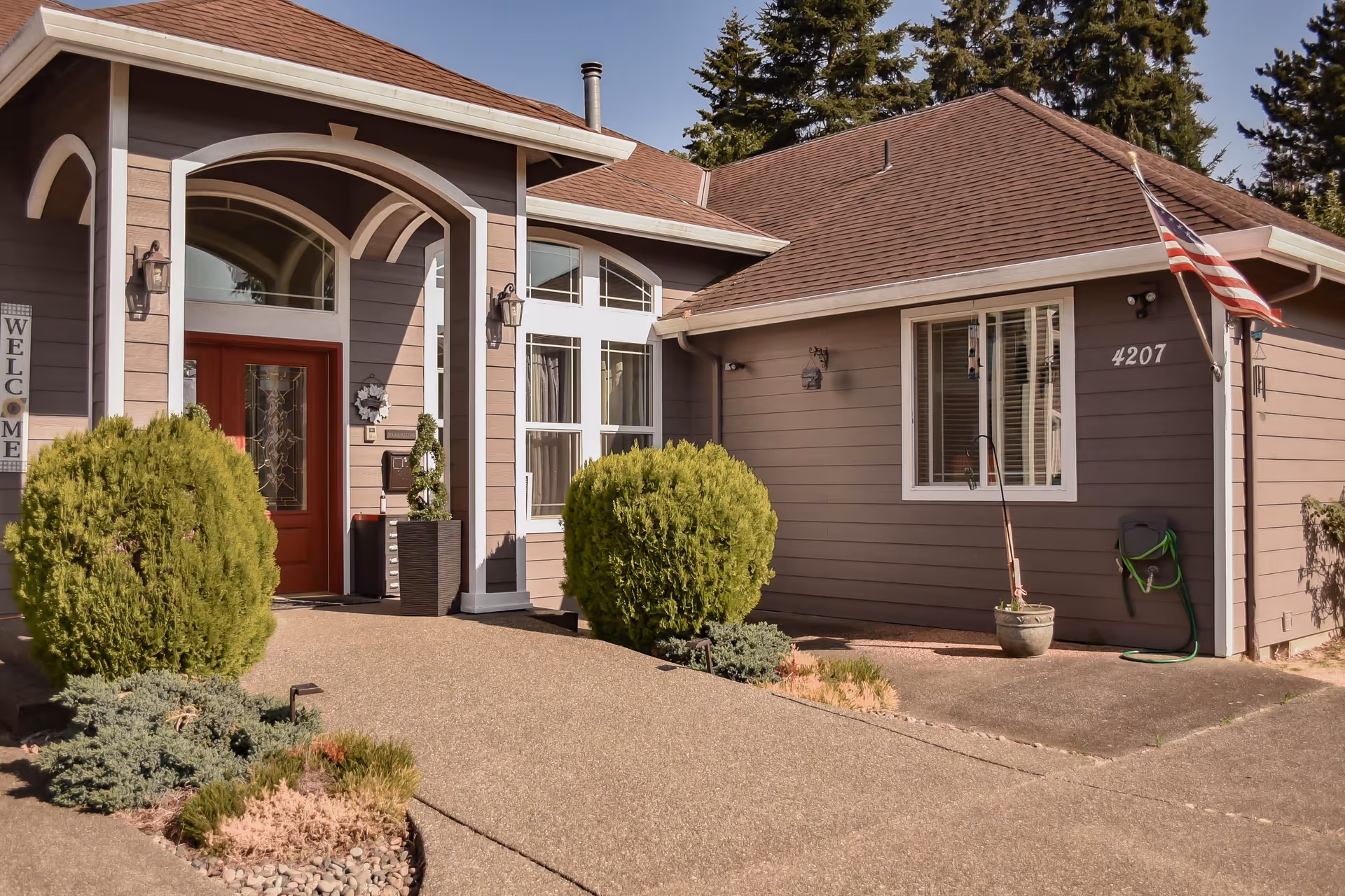 Residential-style senior home exterior with red front door, arched entry, and manicured shrubs.