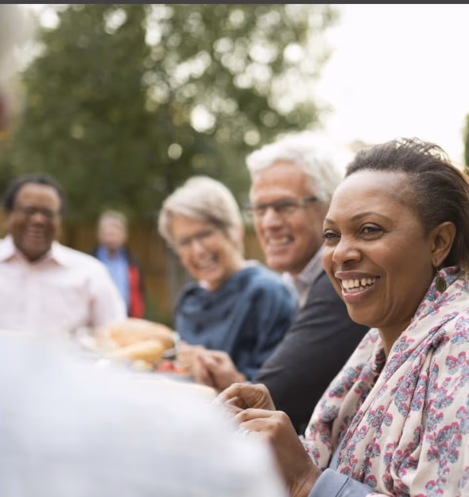 Smiling seniors and caregivers enjoy an outdoor meal together.
