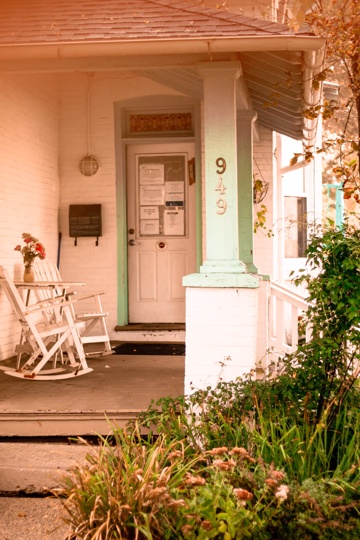 White porch with rocking chairs and potted plants beside a mint-trimmed front door.
