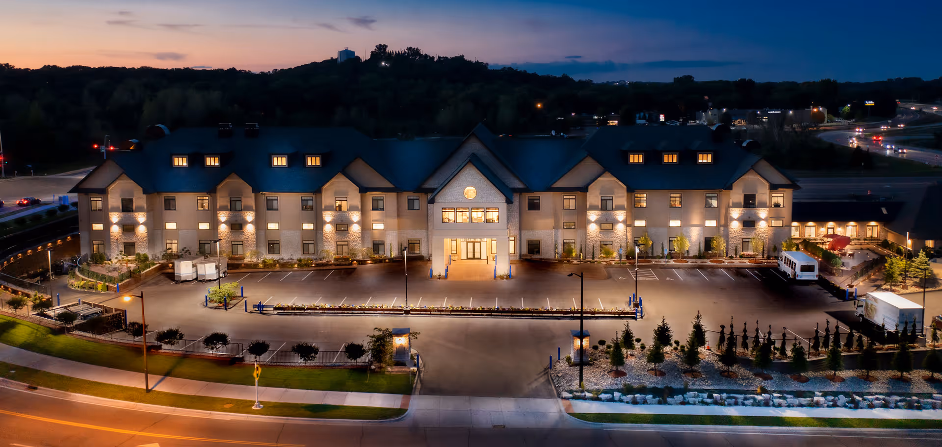 A large memory care building at dusk with illuminated entrance and parking lot.