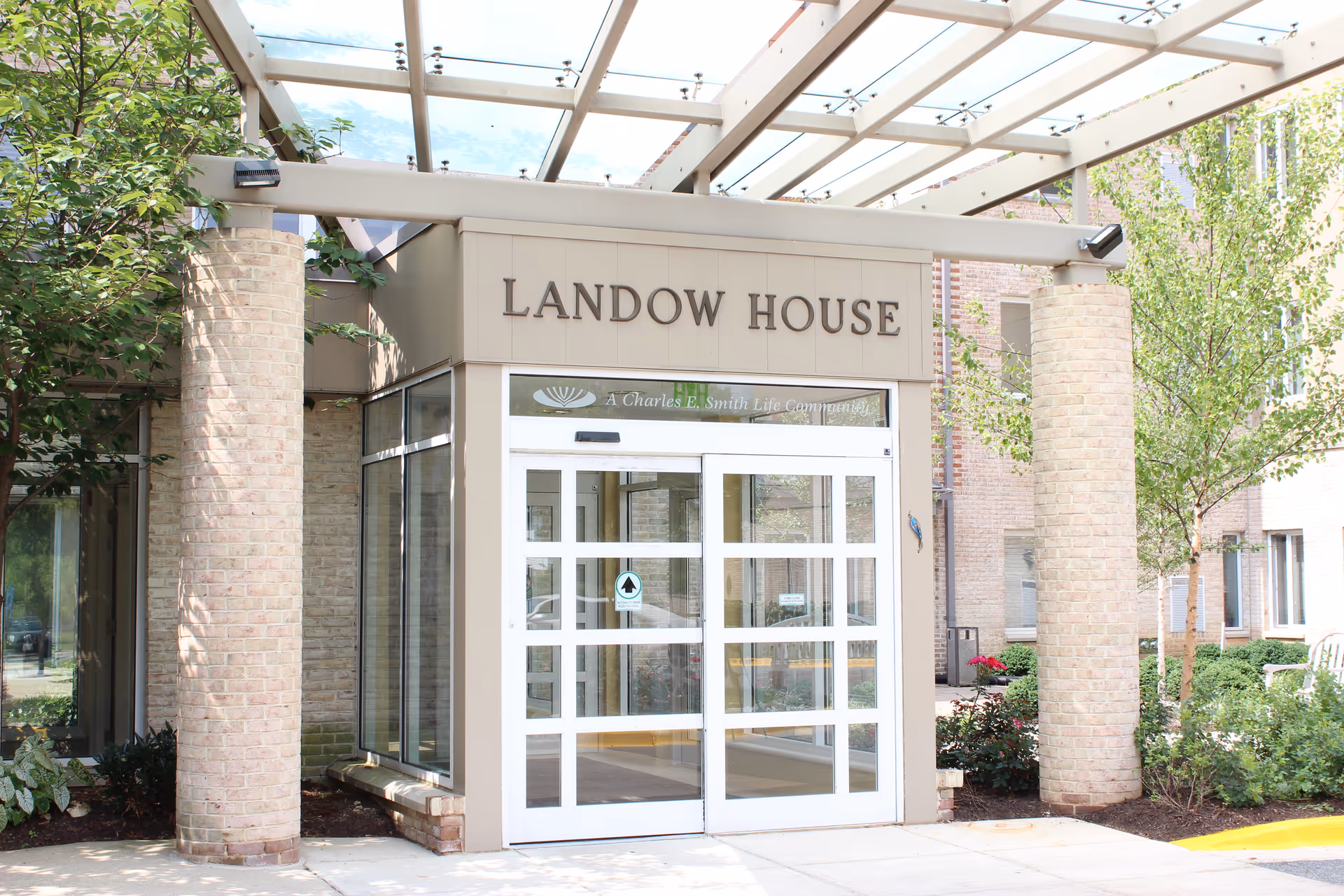Front entrance of Landow House senior living facility with glass doors and brick pillars.