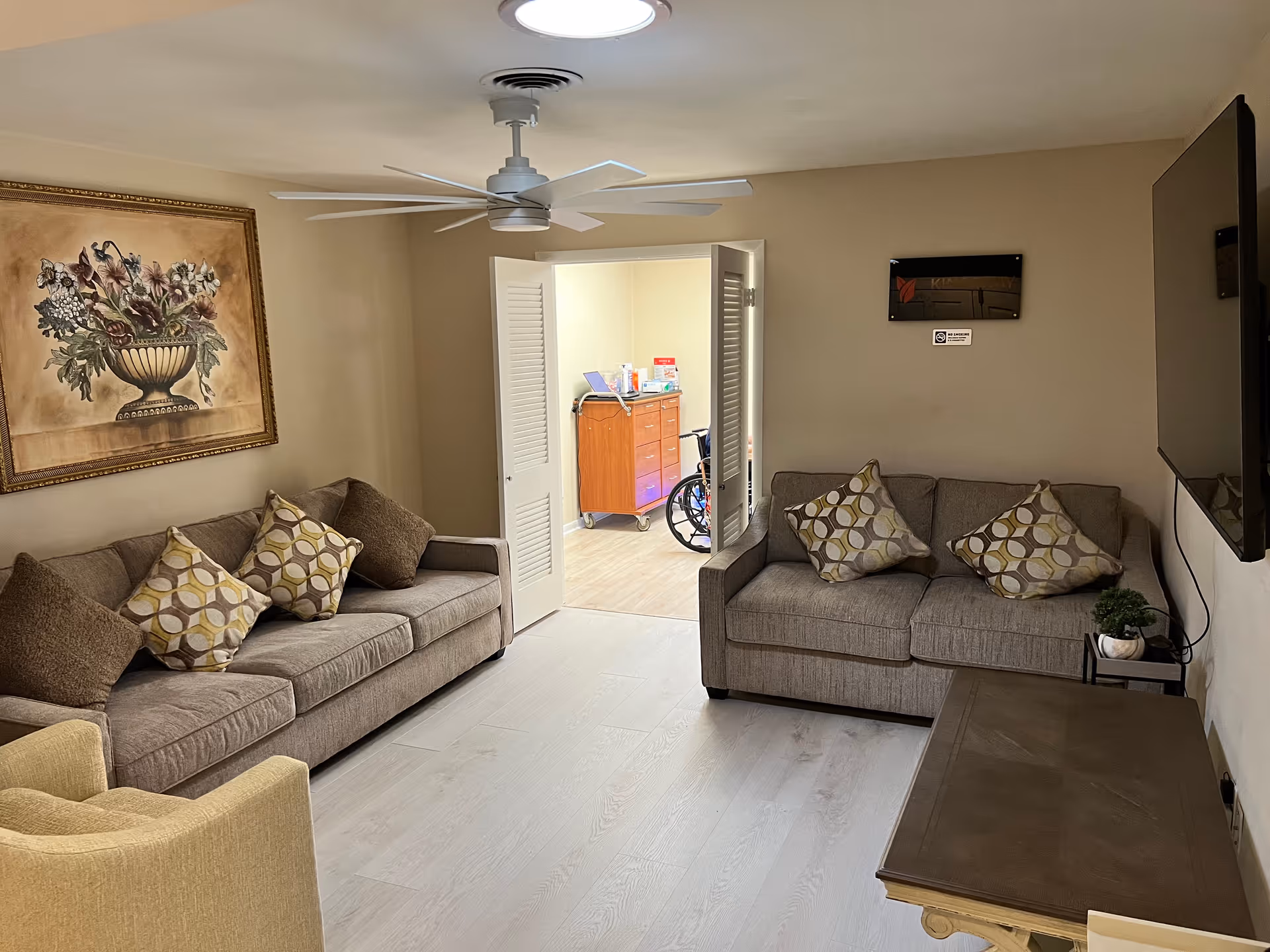 Shared beige living room with two gray sofas, wall art, ceiling fan, and doorway.
