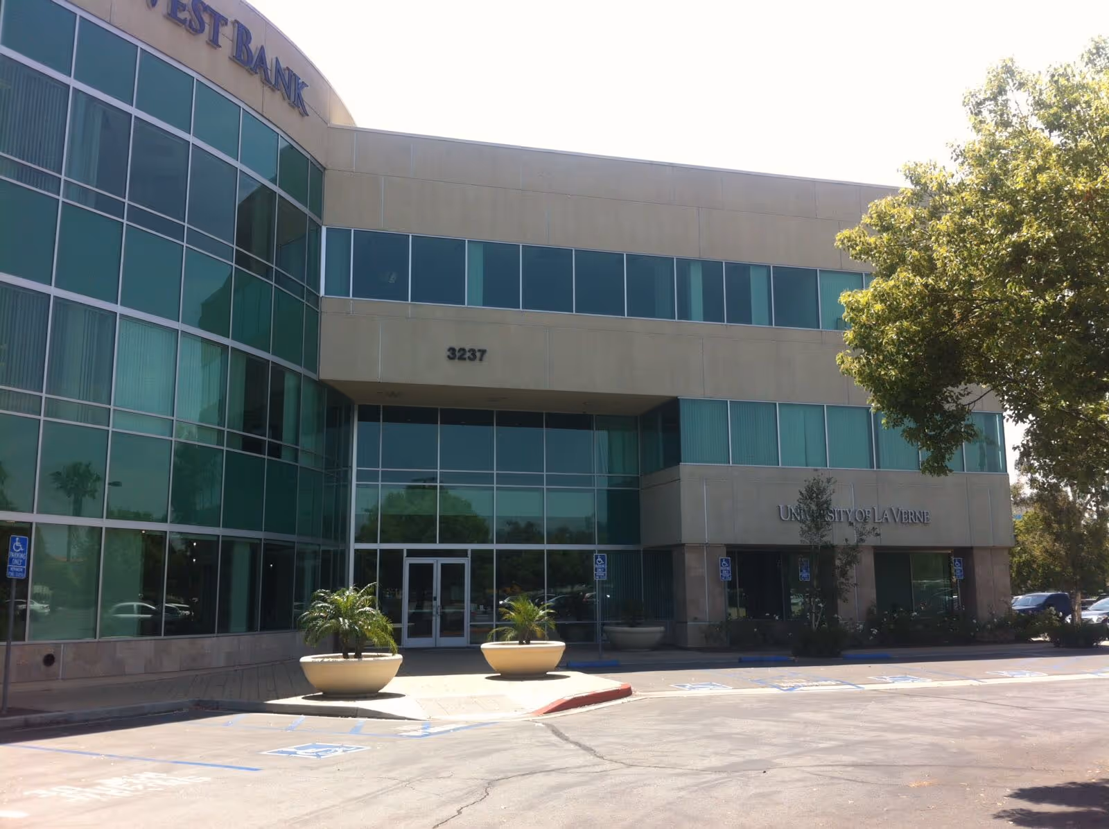 Modern glass-front building with large windows, entryway, and surrounding trees in parking lot.
