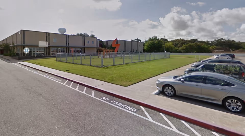 Exterior view of a low-rise healthcare facility with parking and a fenced grassy lawn.