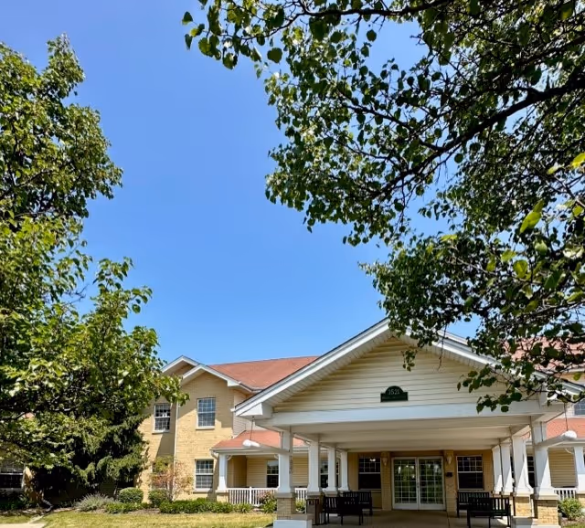 Front exterior of Allure of Zion senior living facility with a covered entrance and benches.