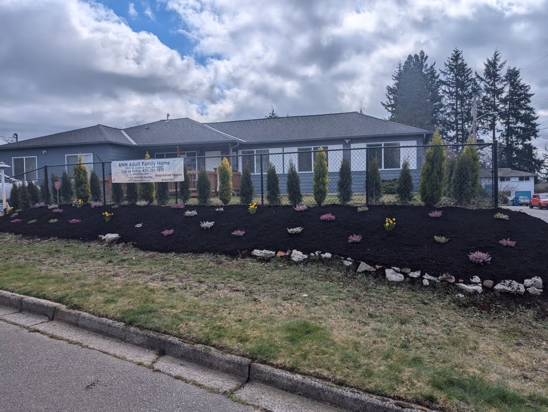 Front exterior of ANN Adult Family Home with a chain-link fence and landscaped bed.
