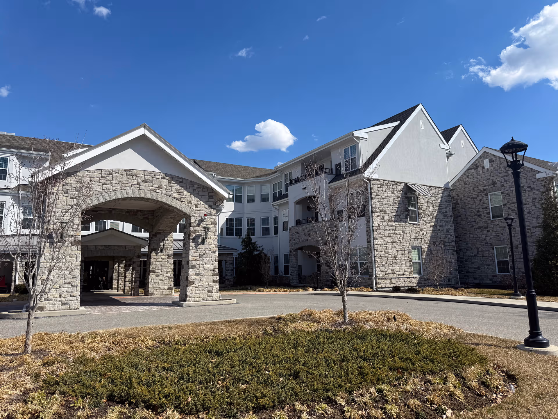 Atria Lafayette Hill exterior with stone facade, arched entrance, under blue sky.
