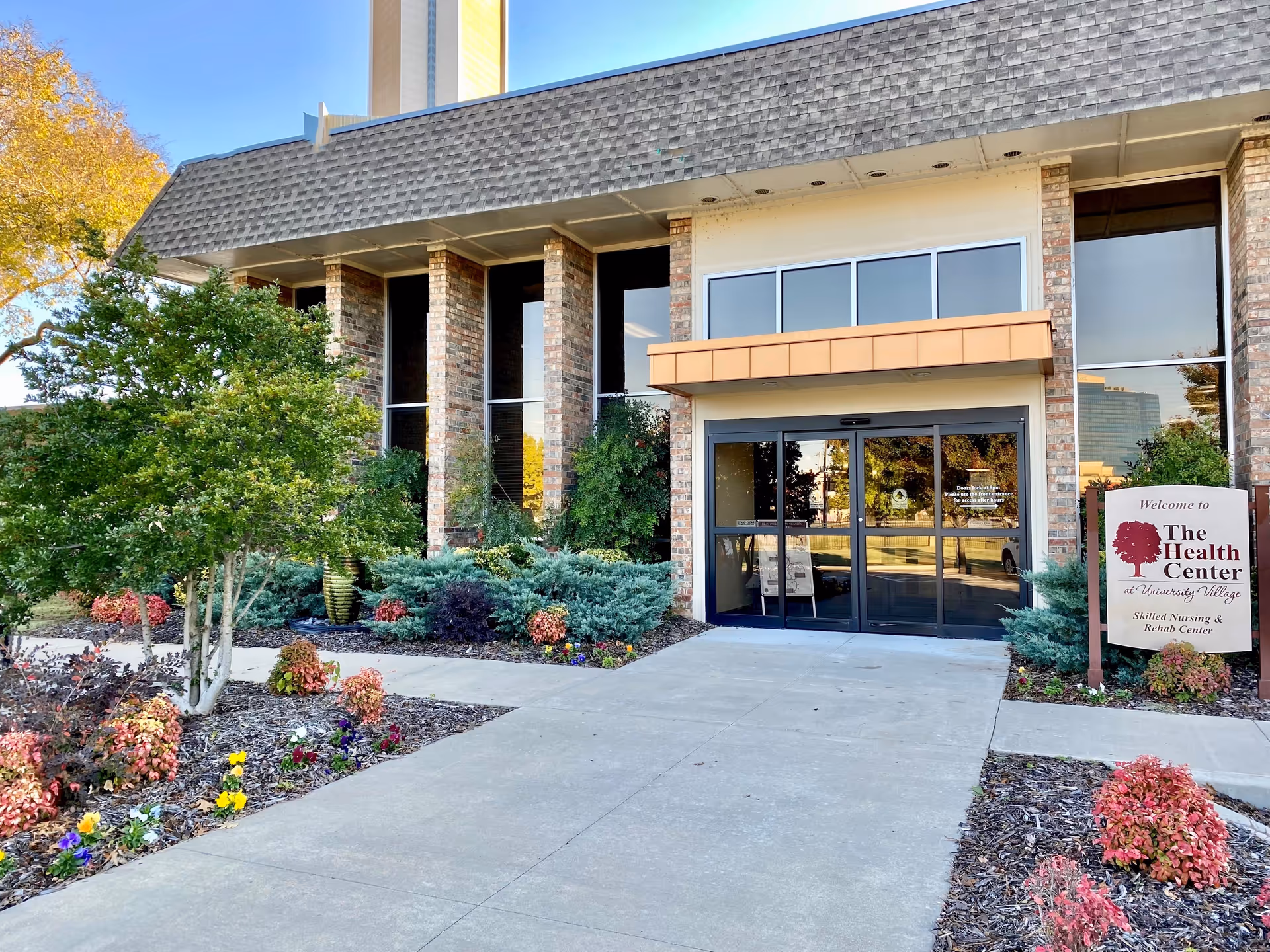 Front entrance of a retirement community with glass doors, brick pillars, and landscaping.