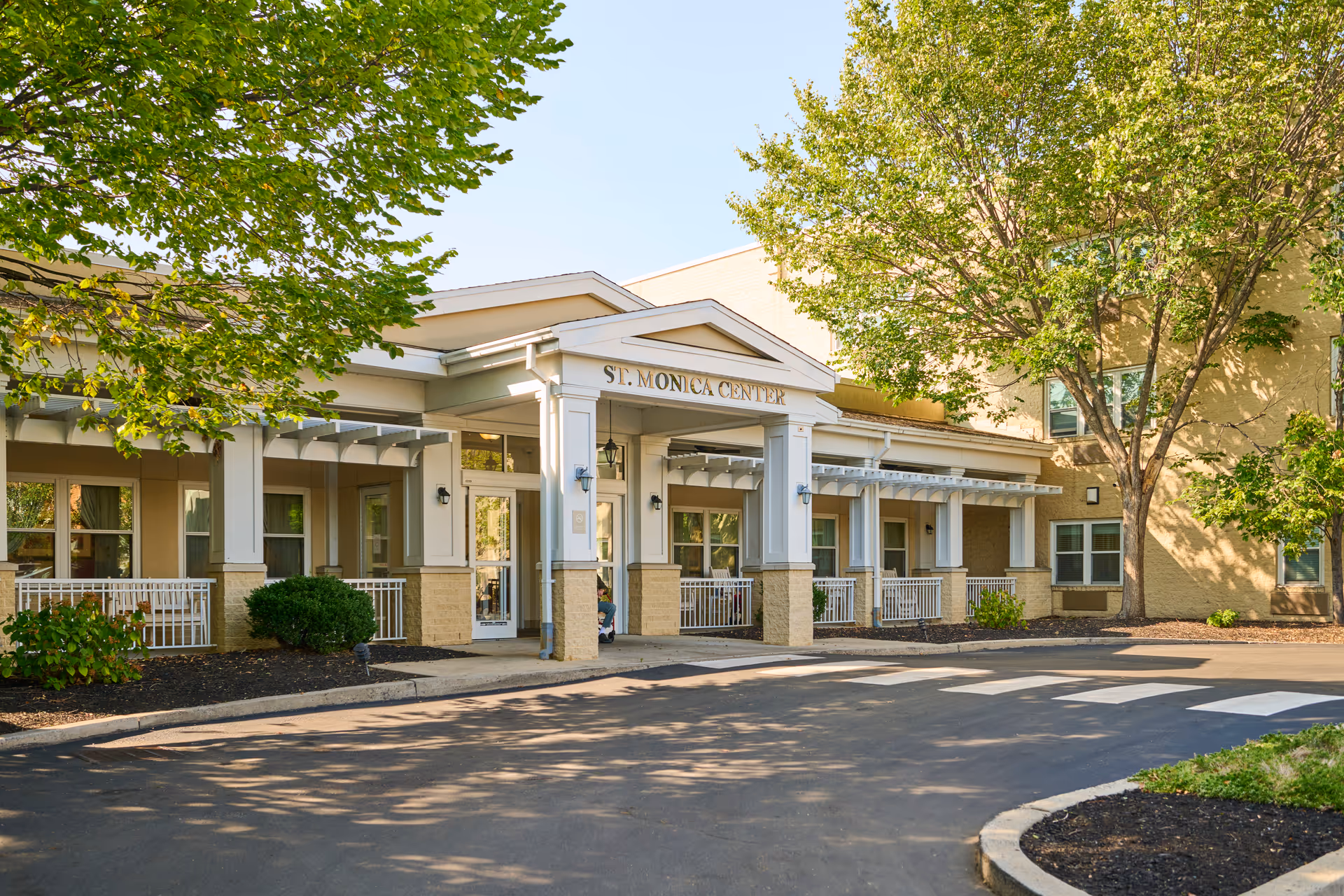 Front view of St. Monica Center entrance with pillars, signage, and surrounding trees.