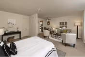 A spacious senior living suite featuring a bed in foreground and cozy seating area.