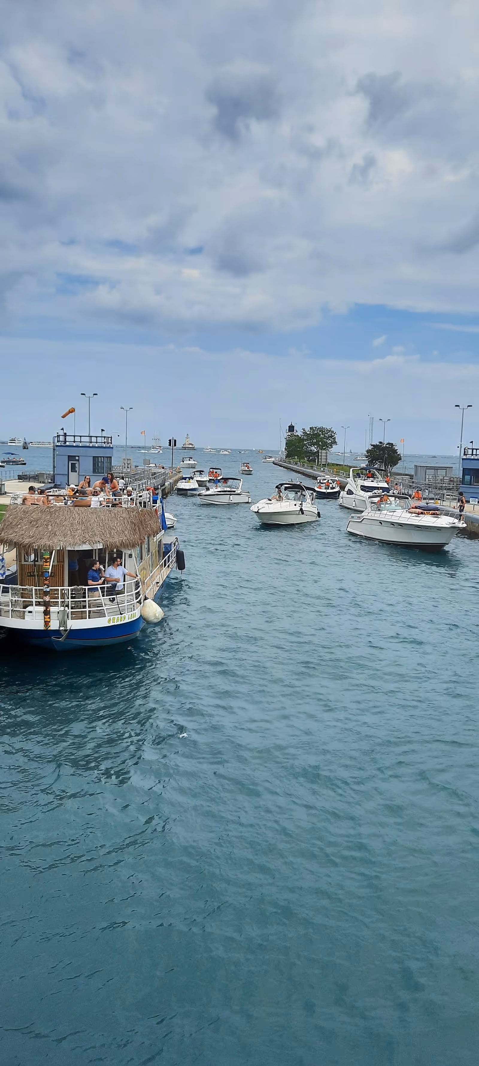 Boats docked at a marina with calm blue water and cloudy sky.