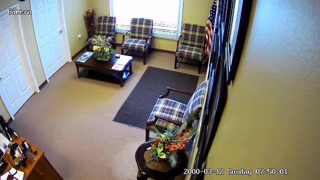 Interior waiting area with plaid chairs, a coffee table, plants, and an American flag.