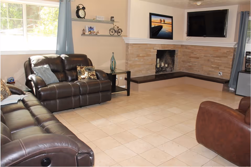 Spacious living room with leather sofas, tiled floor, corner fireplace, wall-mounted TV and a large window.