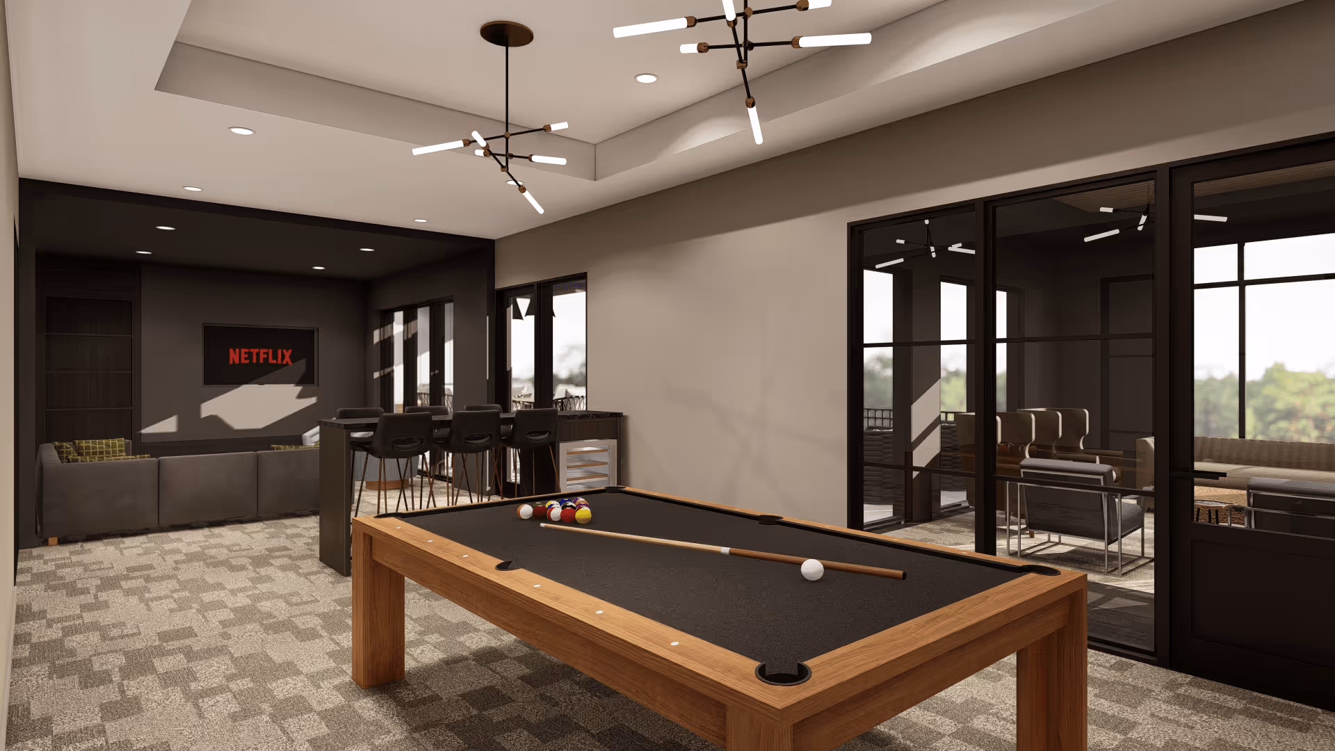 A modern recreational room featuring a pool table with a cue stick and balls arranged on it. In the background, there is a seating area with a large sectional sofa facing a wall-mounted TV displaying the Netflix logo. Next to the sofa is a high counter with bar stools and a small refrigerator underneath. The room has large windows and glass doors leading to another seating area with chairs and sofas, allowing natural light to enter. The ceiling has contemporary light fixtures.