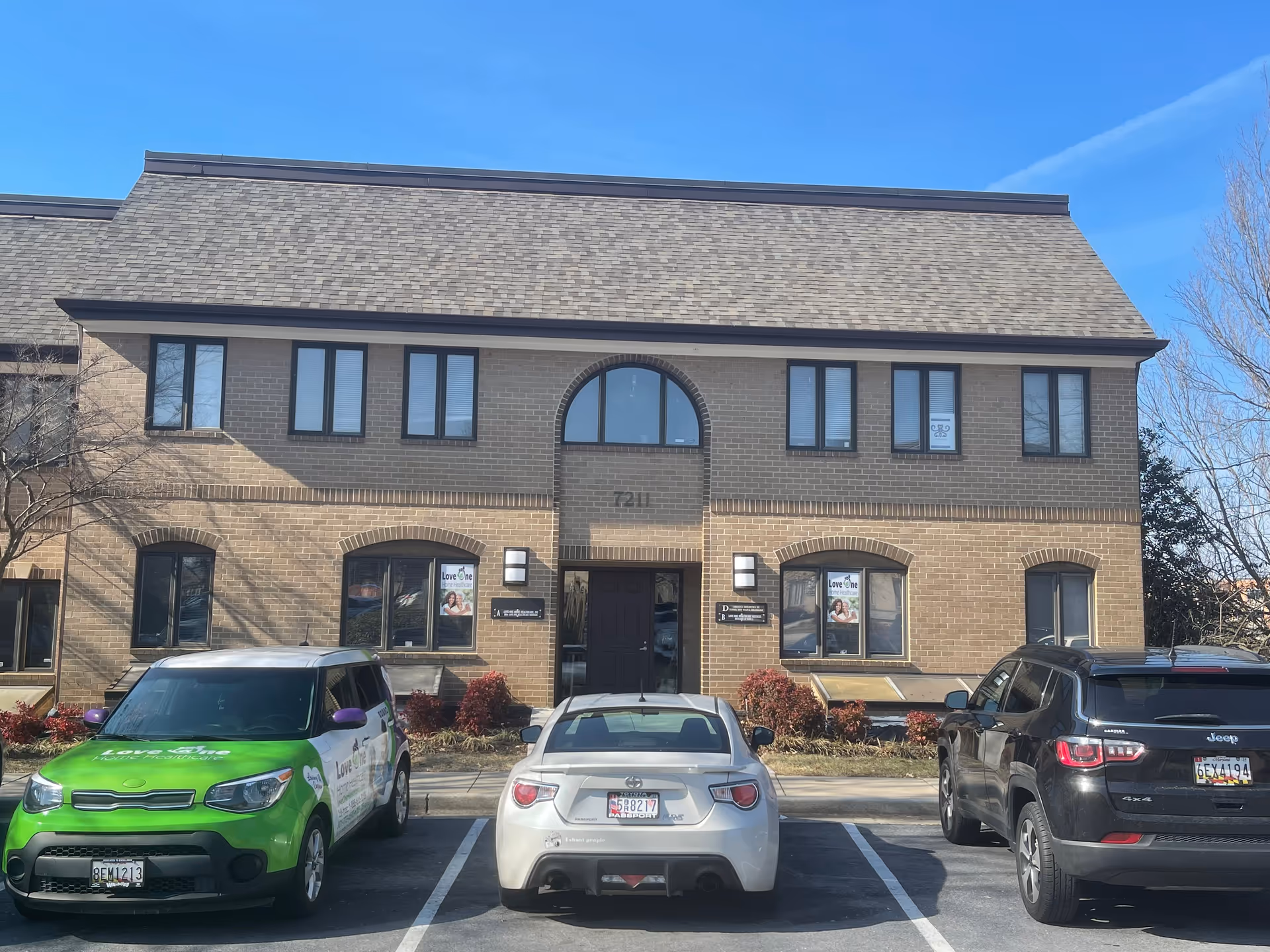 Two-story brick Love One Home Healthcare building with arched entrance and parked cars.