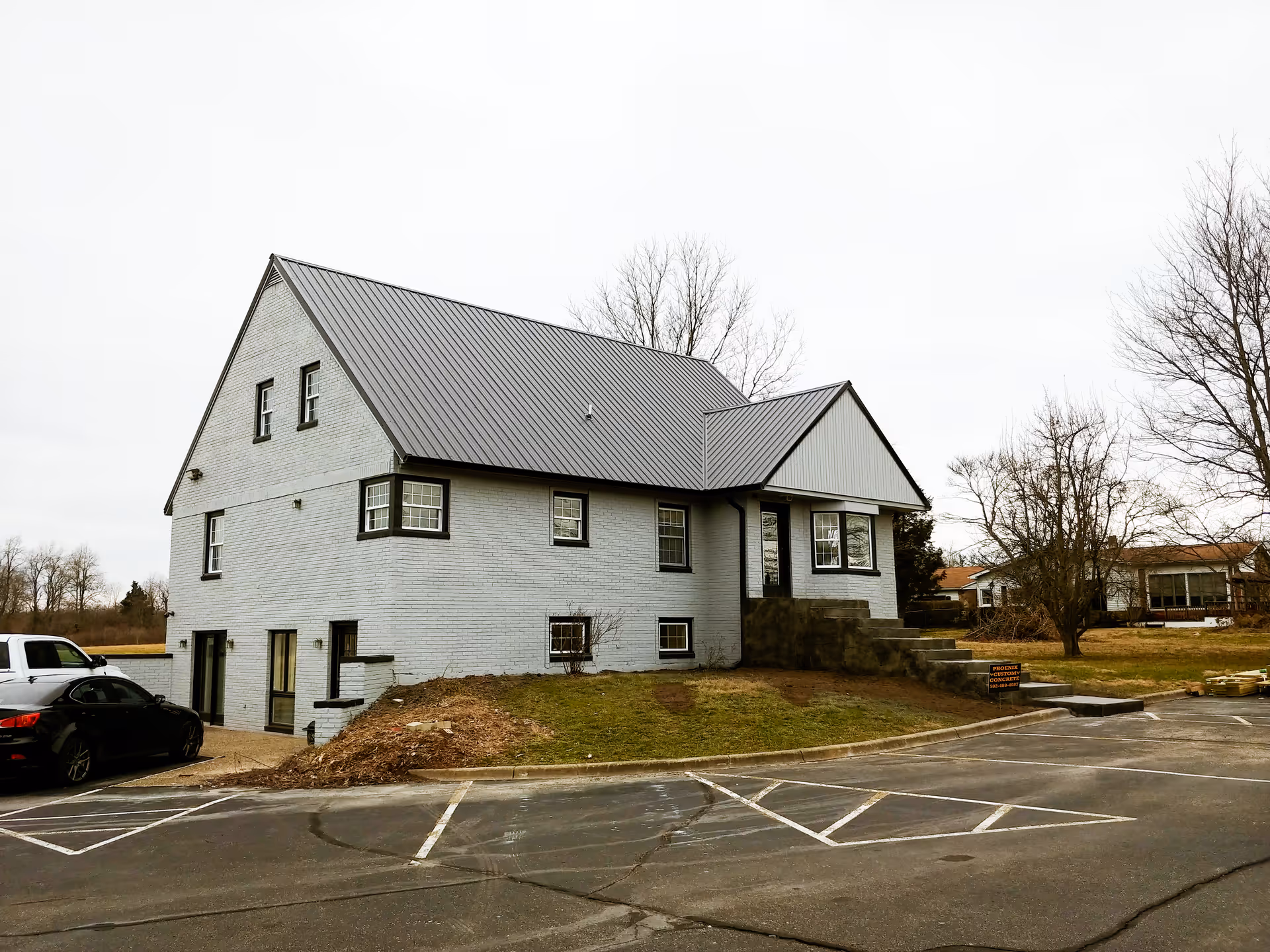 Gray brick senior care building with a metal roof and a parking lot in front.