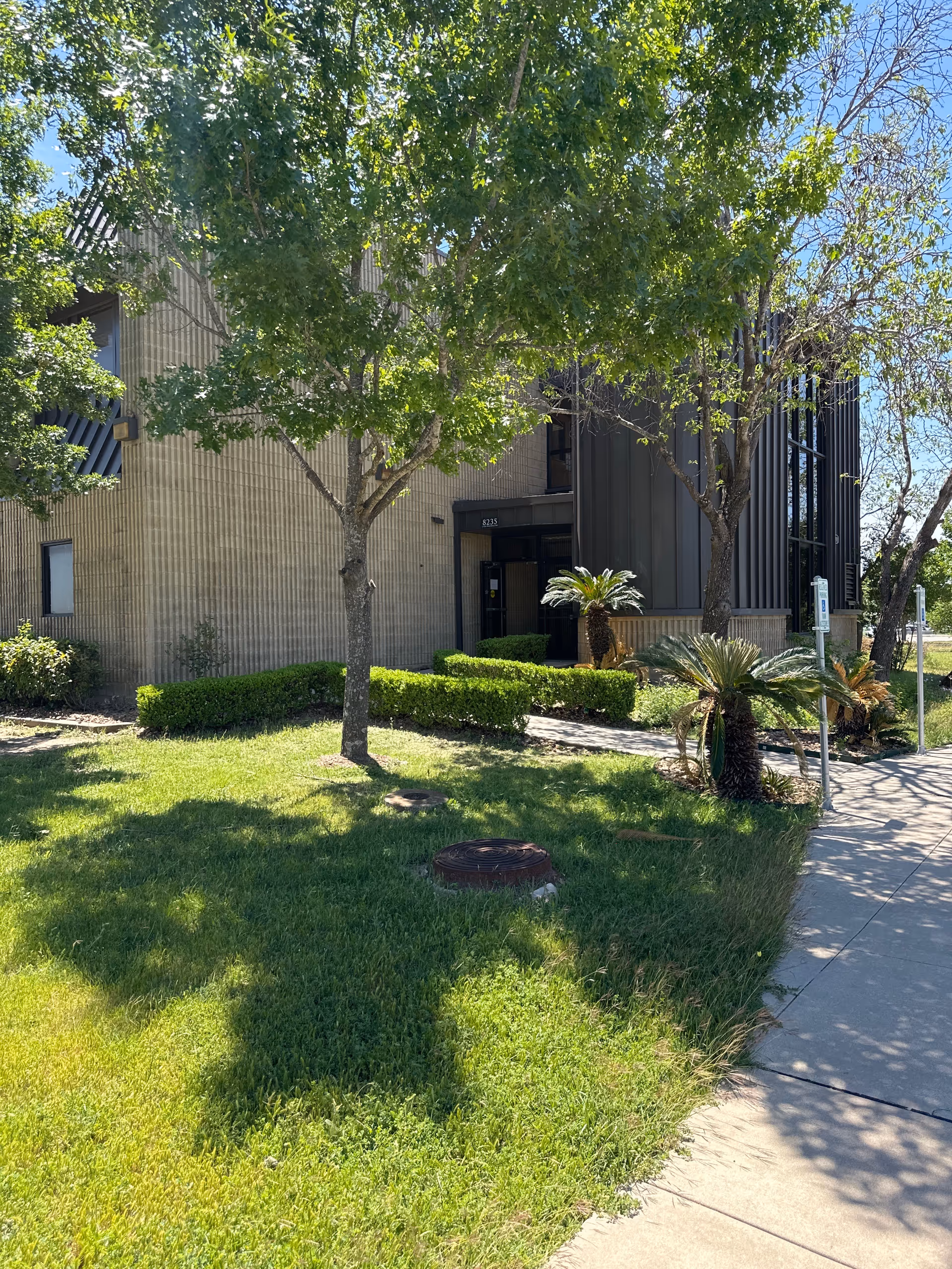 Exterior view of Alegria Primary Home Care building with trees, shrubs, and a sidewalk.