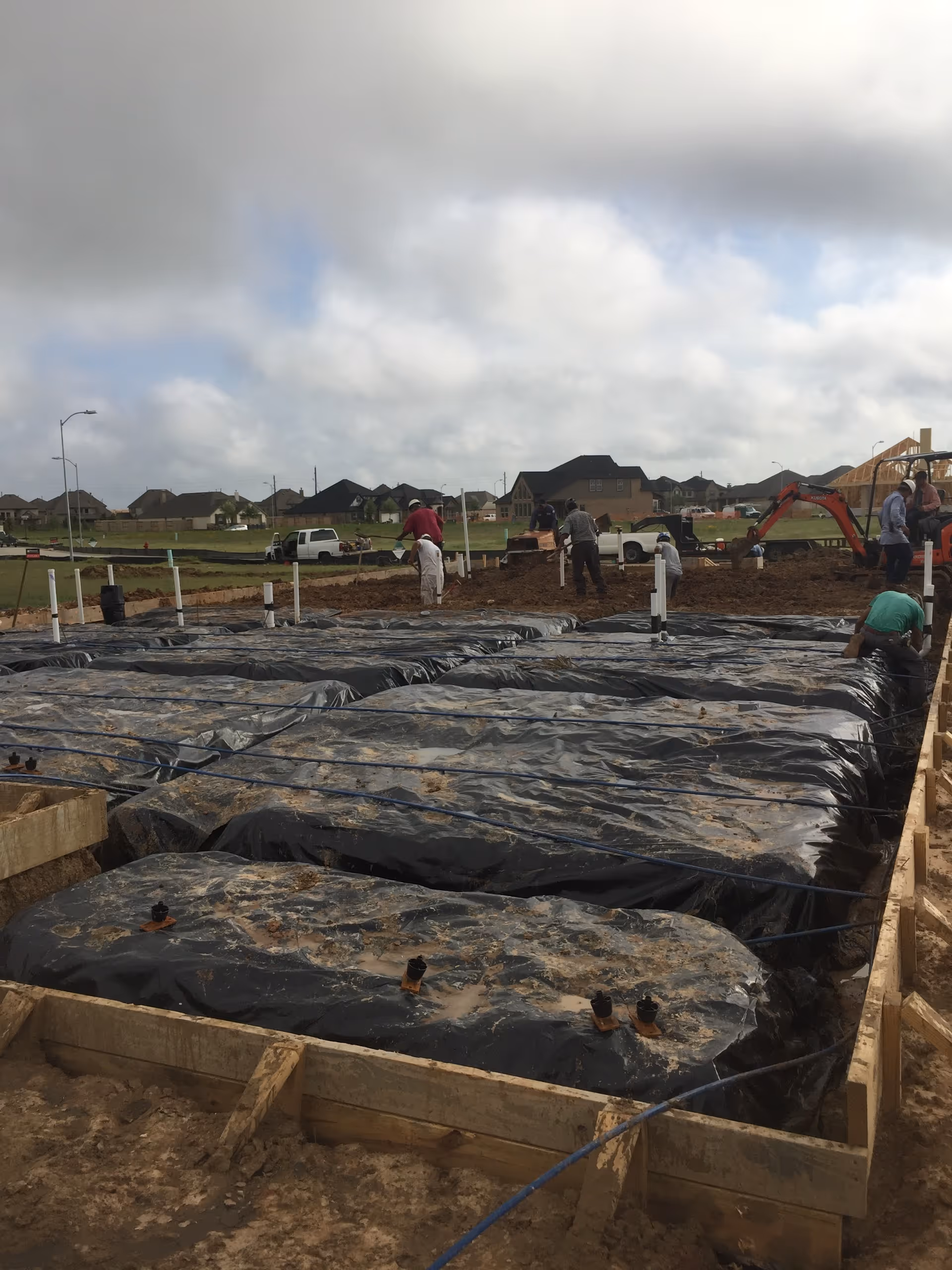 Construction site with workers and large black plastic-covered trenches.