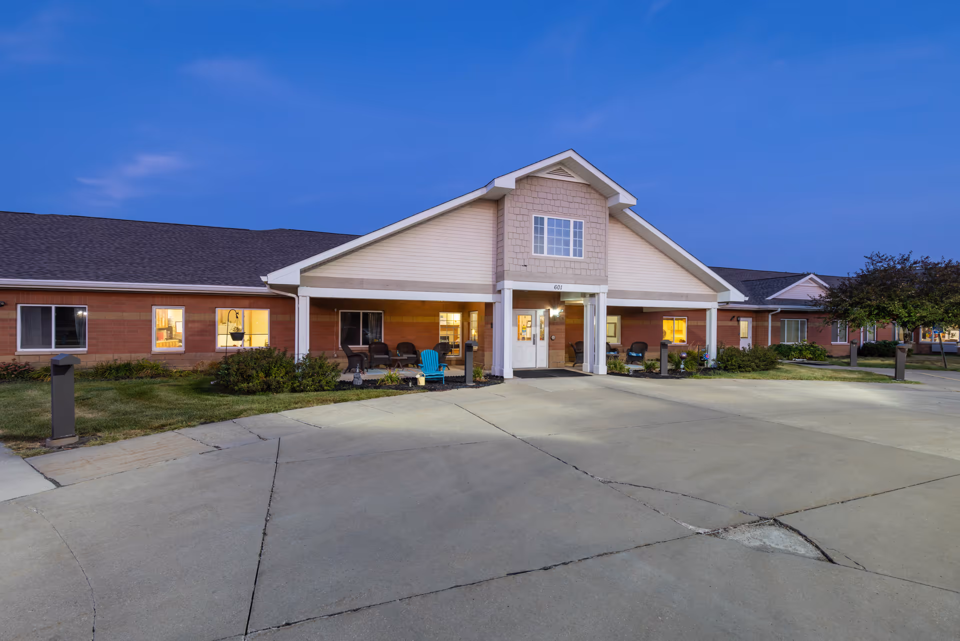 Exterior view of Courtyard Estates at Hawthorne Crossing building at dusk, showing a single-story structure with a covered entrance, outdoor seating, and well-maintained landscaping.