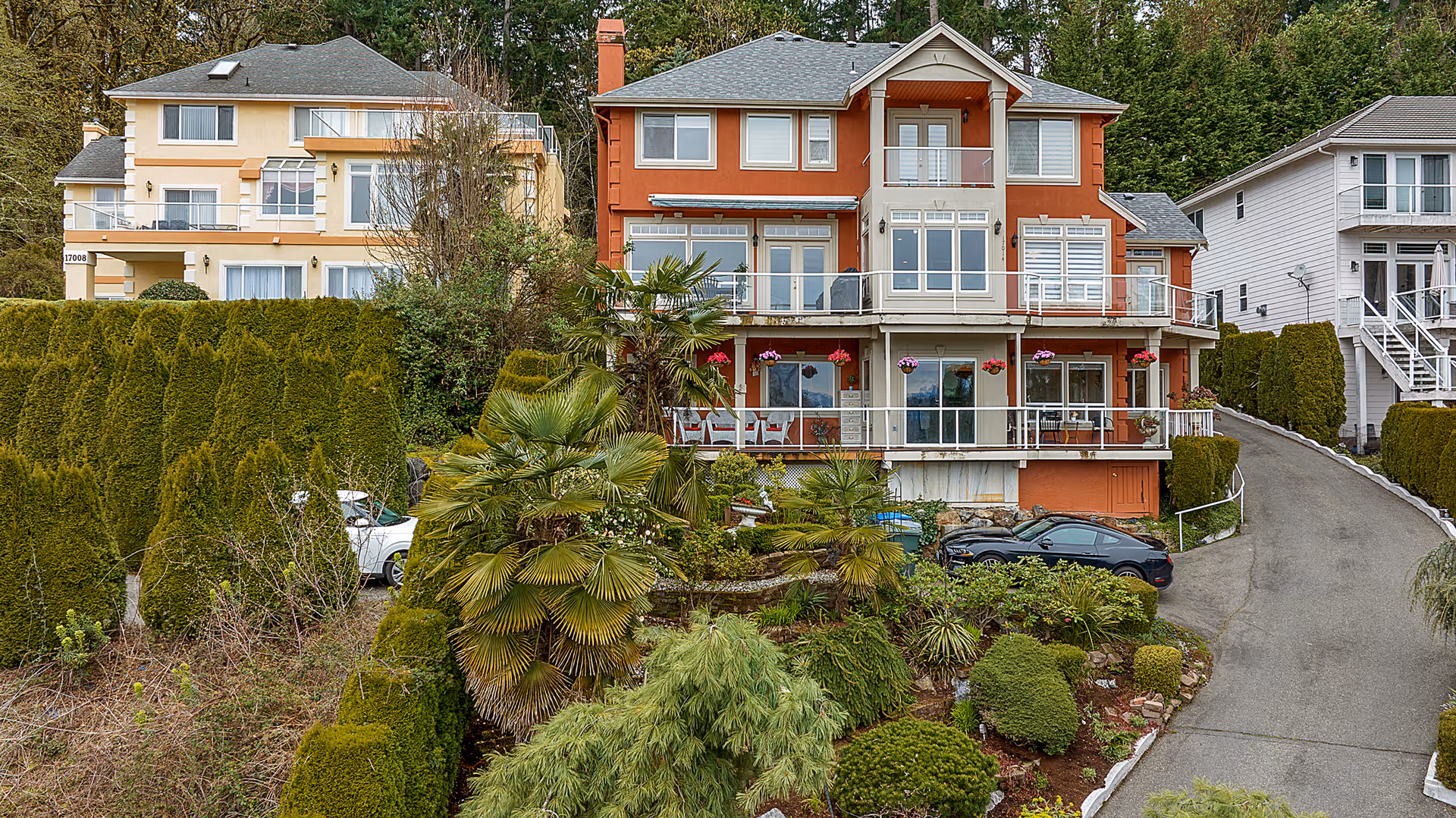 Multi-story residential building with balconies, landscaped yard, and a sloped driveway.