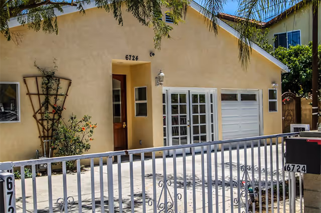 Exterior view of a beige senior living facility front with garage door, gate, and trellis.