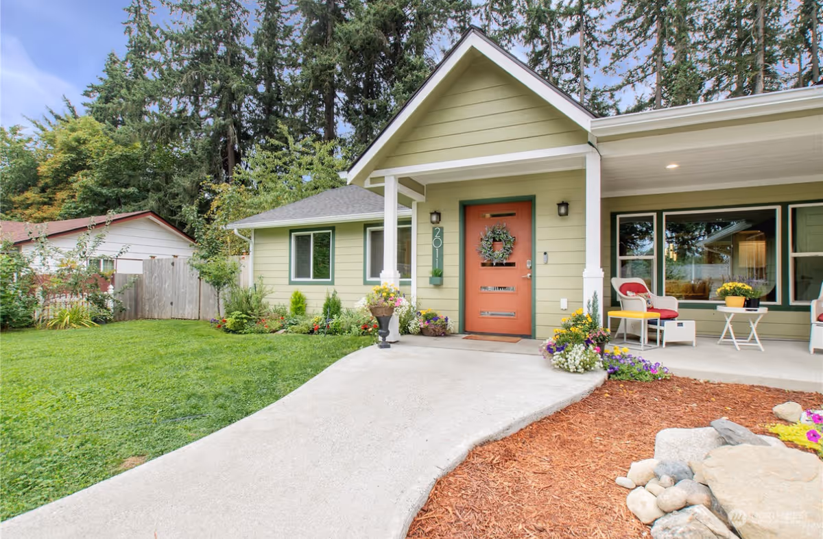 Front view of a green, single-story home with orange door, covered porch, and landscaped yard.