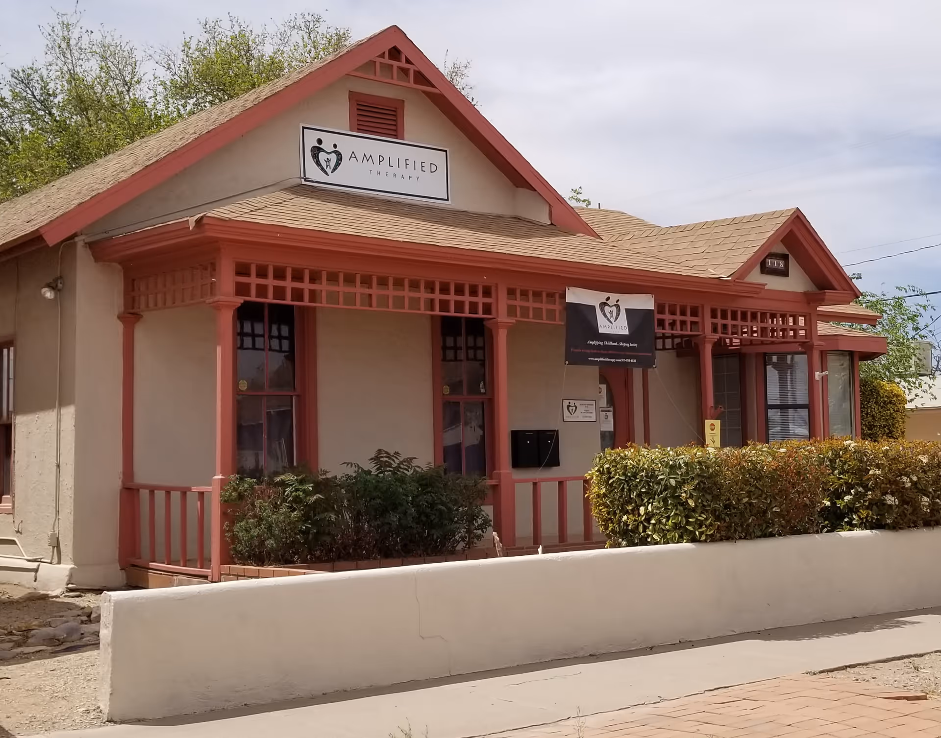 A beige, single-story building with red trim, front porch, and Amplified Therapy sign.