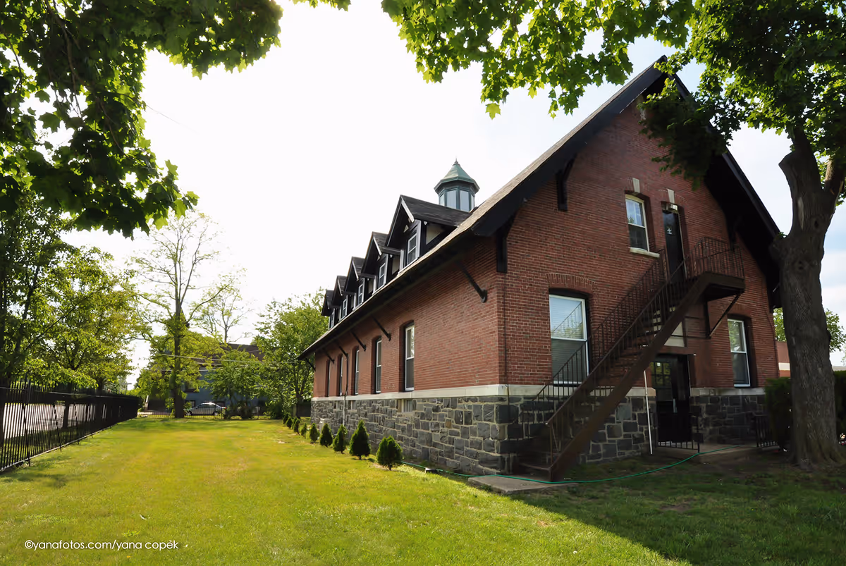 Brick two-story building with an exterior metal staircase, surrounded by a lawn and trees.