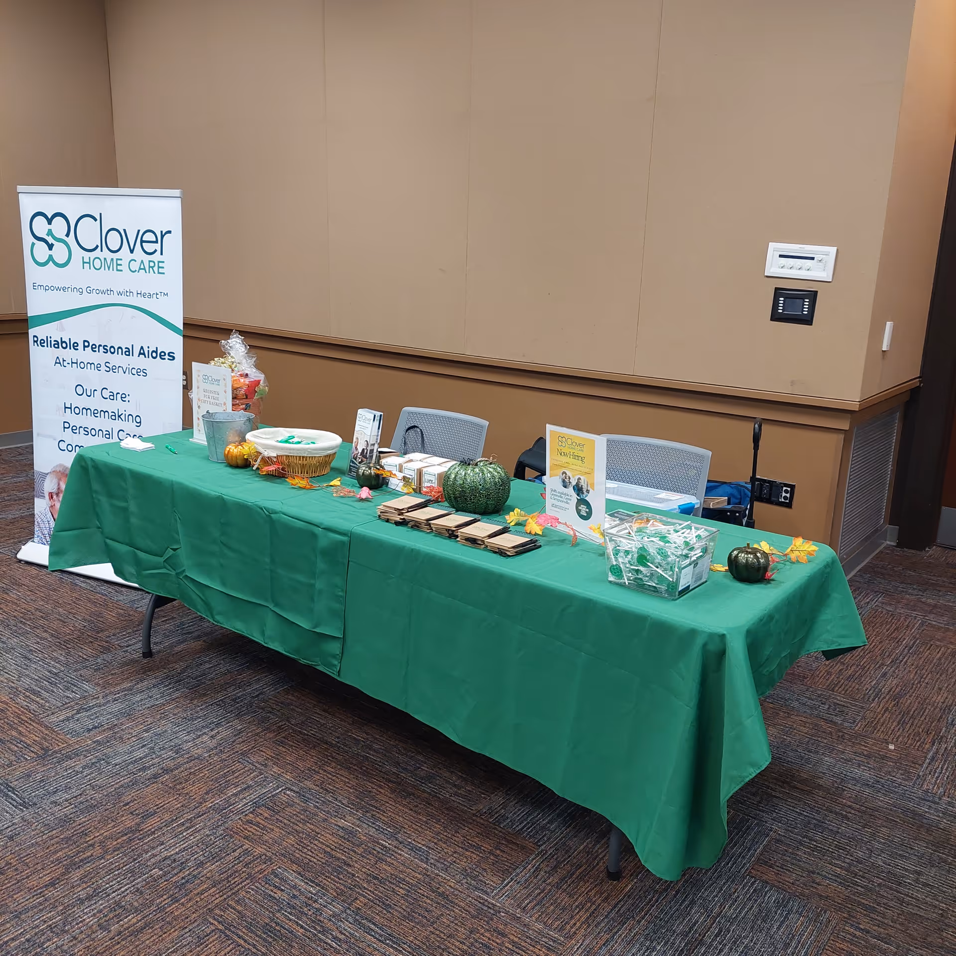 A long table with green cloth and Clover Home Care banner indoors.